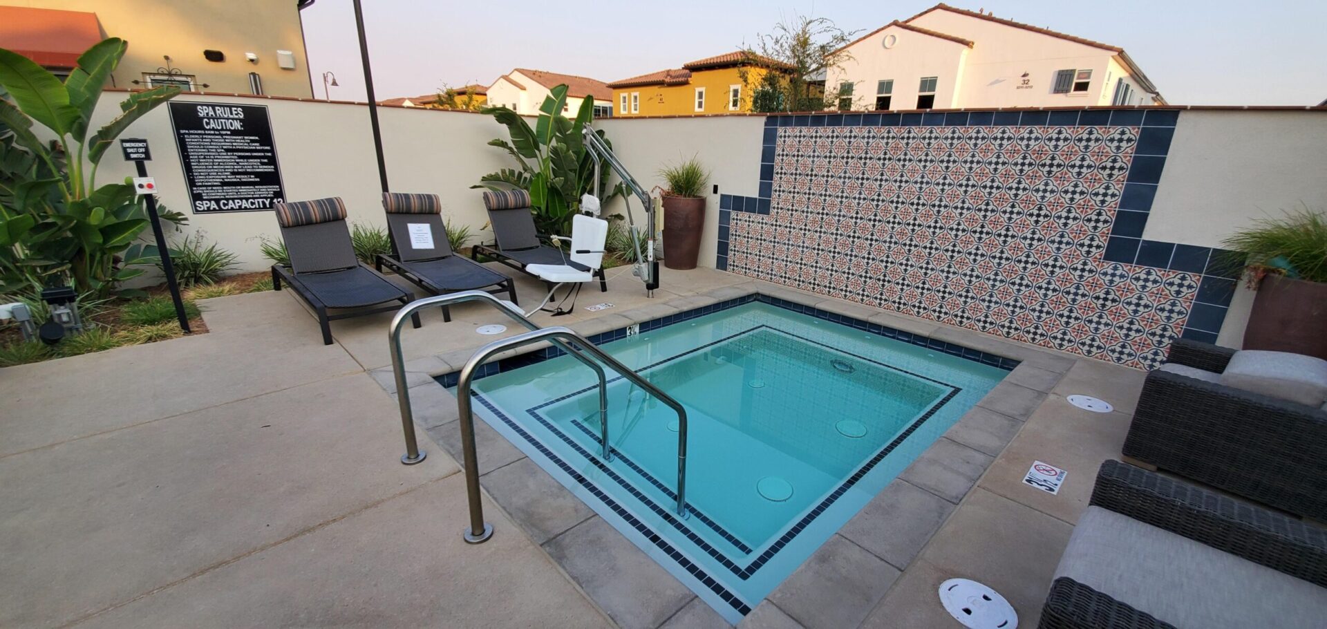 A hot tub with chairs and pool in the background.